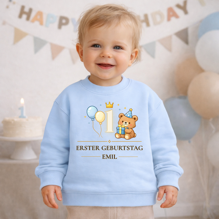 Hellblaues Baby Pullover mit süßem Bärenmotiv, Partyhut, Ballons und der Zahl 1. Der Aufdruck „Erster Geburtstag“ wird mit individuellem Namen personalisiert. Ein süßes Geburtstagsoutfit für Babys und perfektes Geschenk zur ersten Geburtstagsparty.