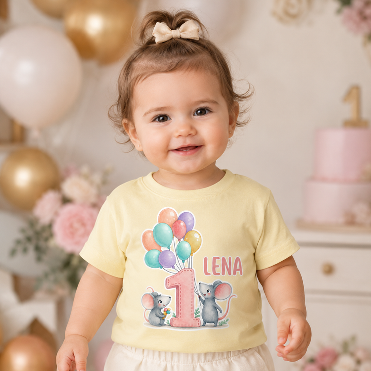 Fröhliches Mädchen trägt ein gelbes personalisiertes Geburtstagsshirt mit rosa Zahl 1, bunten Ballons und Maus Illustration. Der Name Lena macht das Shirt einzigartig für den ersten Geburtstag, Babyfeier oder süße Erinnerungsfotos.