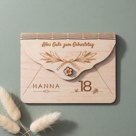 Umschlag Geldgeschenk zum 18. Geburtstag mit Motiv Trockenblumen, getrockneten Gräsern und Ähren. Graviert sind HANNA über drei Herzen und die 18, jede Zahl von 18 bis 99 ist möglich. Auf salbeigrünem Grund.