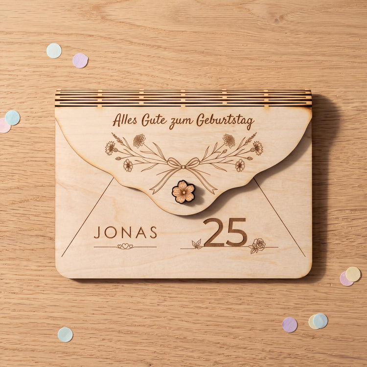 Gutschein Verpackung aus Holz zum 25. Geburtstag, Motiv Wiesenblumen mit Kornblumen und Gräsern. Name JONAS über drei Herzen und Zahl 25 graviert; Gutscheinkarten und Euro-Scheine bis 100 Euro liegen flach darin.