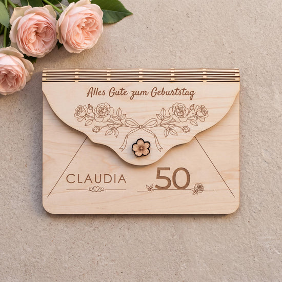 Personalisierter Holzumschlag zum Geburtstag mit Motiv Rosen, einem Bogen aus Gartenrosen mit Schleife. Graviert: Alles Gute zum Geburtstag, Name CLAUDIA über drei Herzen und die Zahl 50. Größe 170 x 120 mm.