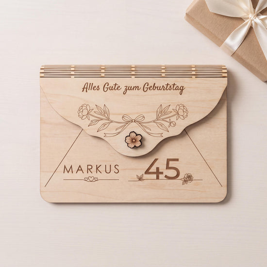 Originelles Geldgeschenk zum 45. Geburtstag: Holzumschlag mit Motiv Pfingstrosen und Schleife, Name MARKUS über drei Herzen. Auf Bestellung graviert, Bearbeitungszeit 2 Werktage. Neben einem Geschenk in Kraftpapier.