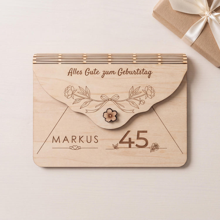 Originelles Geldgeschenk zum 45. Geburtstag: Holzumschlag mit Motiv Pfingstrosen und Schleife, Name MARKUS über drei Herzen. Auf Bestellung graviert, Bearbeitungszeit 2 Werktage. Neben einem Geschenk in Kraftpapier.