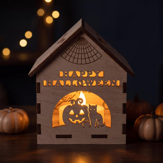 Happy Halloween Laterne aus Holz am Abend, der zweizeilige Schriftzug leuchtet warm, kleine Kürbisse daneben