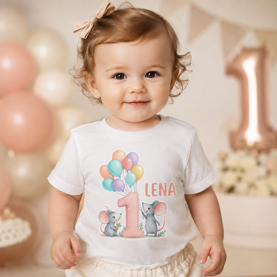Kleines Mädchen trägt ein personalisiertes weißes Babyshirt mit rosa Zahl 1, bunten Luftballons und süßen Mäusen. Der Name Lena ist aufgedruckt. Perfektes Outfit für den ersten Geburtstag, Cake Smash Shooting oder Baby Party im niedlichen Pastell Stil.